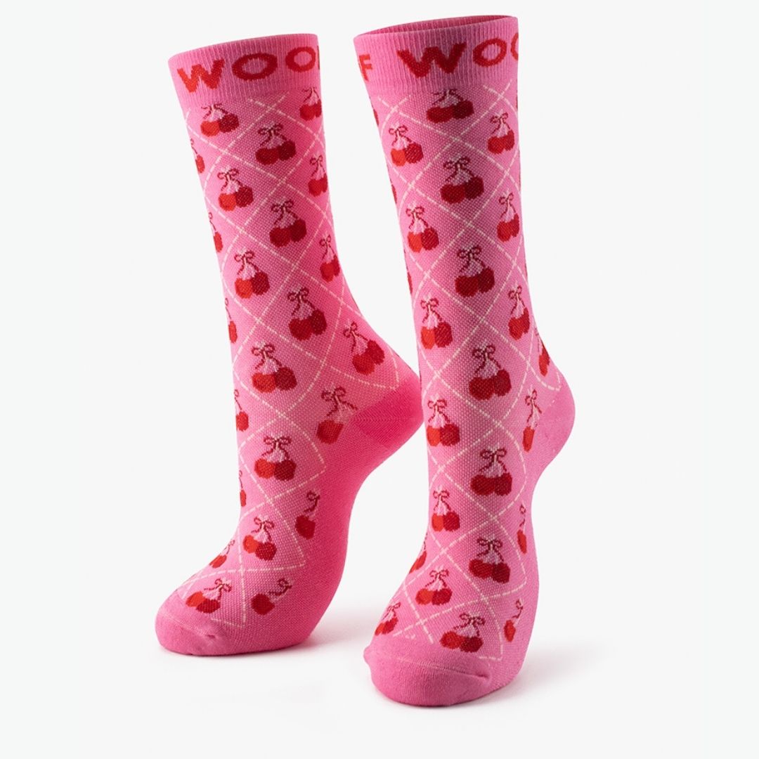 A bright pink Cherry Bows Bamboo Crew Compression Socks standing upright, featuring a white diamond grid pattern filled with red cherry clusters and bow accents, complete with dark pink "WOOF" woven into the top cuffs.  